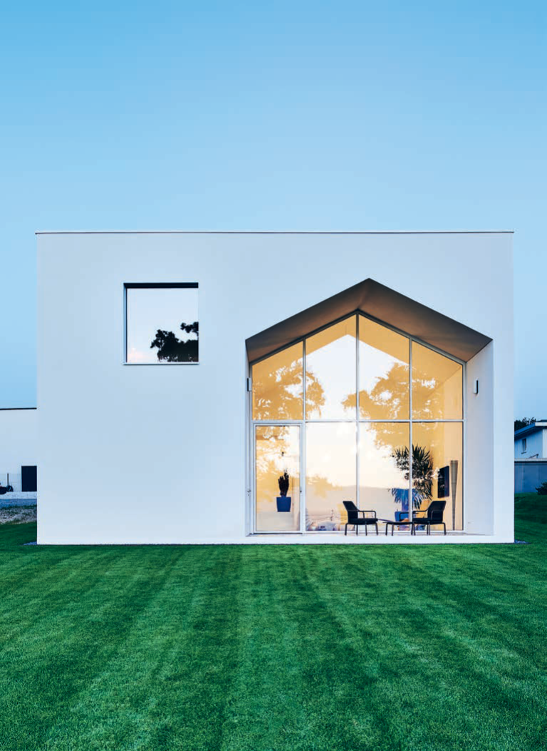 Die grosse Öffnung zeichnet die Silhouette eines Hauses mit Satteldach nach. Durch ihre zurückversetzte Positionierung neben dem quadratischen Fenster wirkt diese Fassade wie ein Puzzledeckel eines Spielkastens für Bausteine.