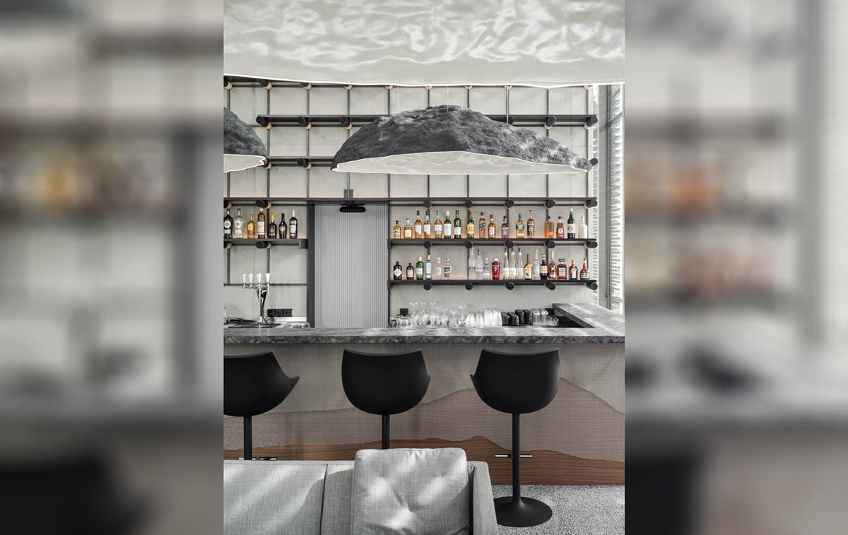 Bar des Hotels Horlogers, drei Stühle stehen vor einer Theke. Dahinter zahlreiche Flaschen gefüllt mit Spirituosen.
