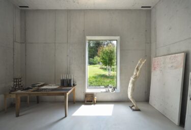 Das Atelier ist mit rohem Beton rauer als das Wohnhaus. Tageslicht und der Gartenblick wirken besänftigend, wobei die Öffnung auch ein Fenster zur Inspiration ist.