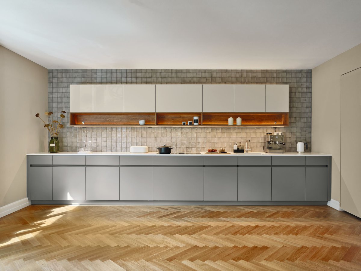 Ein eleganter Materialmix prägt die Küche: Fischgrätparkett, warme Naturfarben und Fliesen in Steinoptik verleihen dem Raum einen warmen, leicht rustikalen Look.