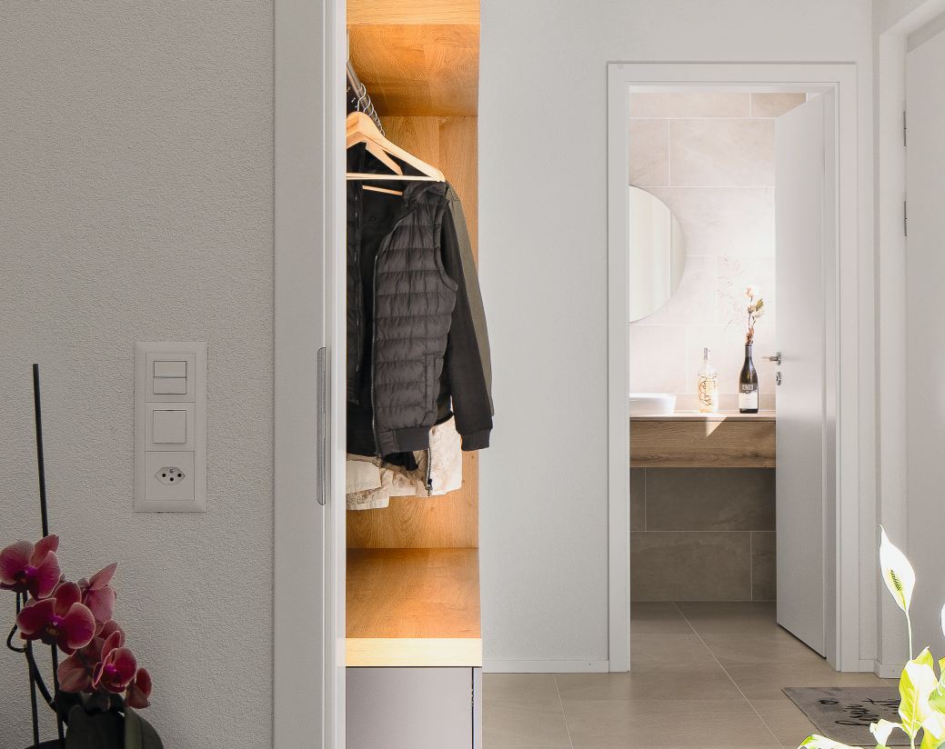 Entrée mit integrierter Garderobe und Blick in ein modernes Badezimmer.
